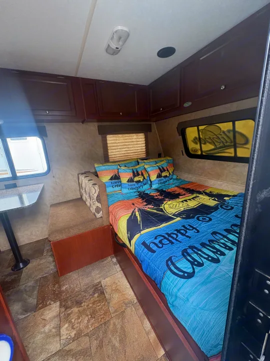 RV rental interior: cozy bedroom featuring "happy camper" bedding, storage cabinets, and a dining nook with a window.. Coachmen Clipper 17BH 2015