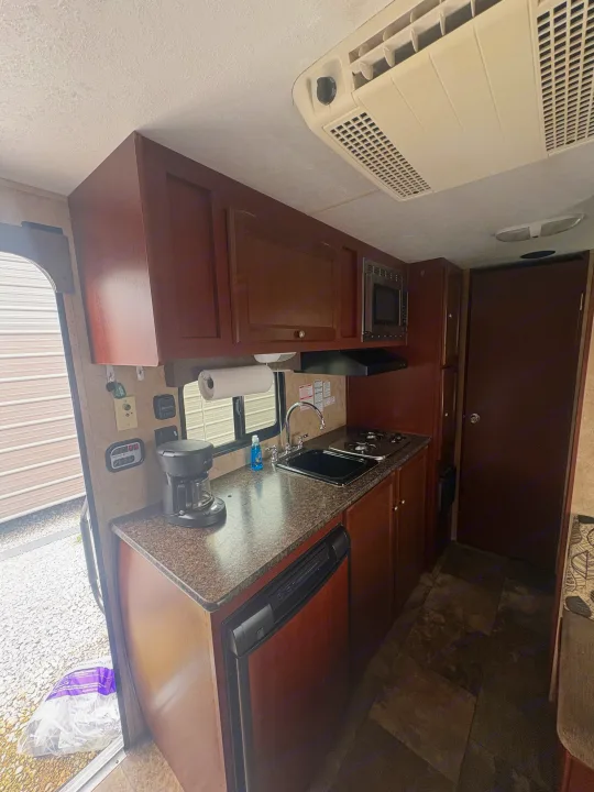 RV rental kitchen: compact design with dark wood cabinets, sink, stove, microwave, and ceiling AC unit for comfort.. Coachmen Clipper 17BH 2015