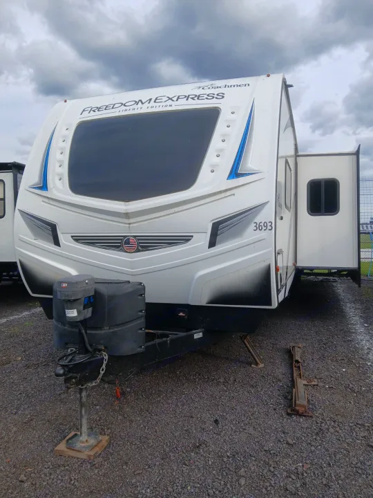 White Coachmen Freedom Express travel trailer RV rental with slide-out extended, parked on gravel under a cloudy sky.. Coachmen Other 2021