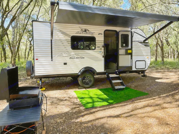 This Jay Flight Baja Edition rv rental is ready for adventure! Parked in a wooded campsite, featuring an awning, steps, and outdoor griddle.. Jayco Jay Flight SLX 175 FQW Baja 2026