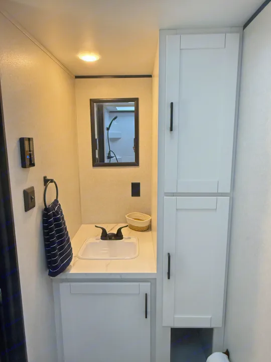 A bright, compact bathroom in an RV rental, showing a sink, mirror, towel, modern cabinetry, and integrated controls.. Jayco Jay Flight SLX 175 FQW Baja 2026