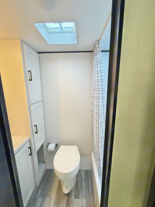 This compact rv rental bathroom features a white toilet, gray wood-look floor, shower curtain, and built-in storage cabinets.. Jayco Jay Flight SLX 175 FQW Baja 2026