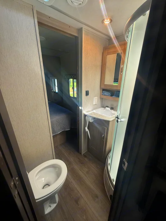 Inside a bright RV rental: compact bathroom with toilet, sink, and shower, offering a glimpse into the adjoining bedroom.. Coachmen Other 2021
