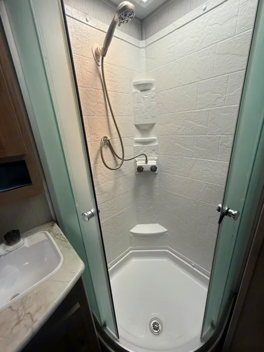 This RV rental's compact bathroom features a corner shower with a handheld showerhead and a small sink.. Coachmen Other 2021
