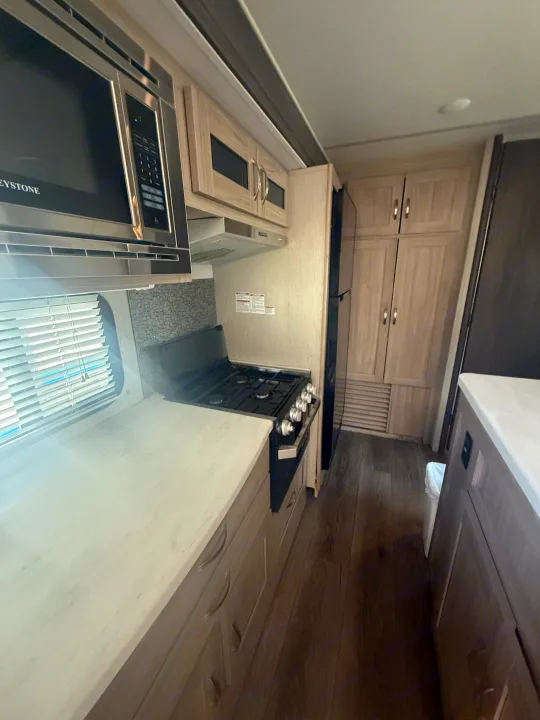 Inside an RV rental: a modern kitchen with microwave, gas stove, light wood cabinets, fridge, and white countertops.. Coachmen Other 2021