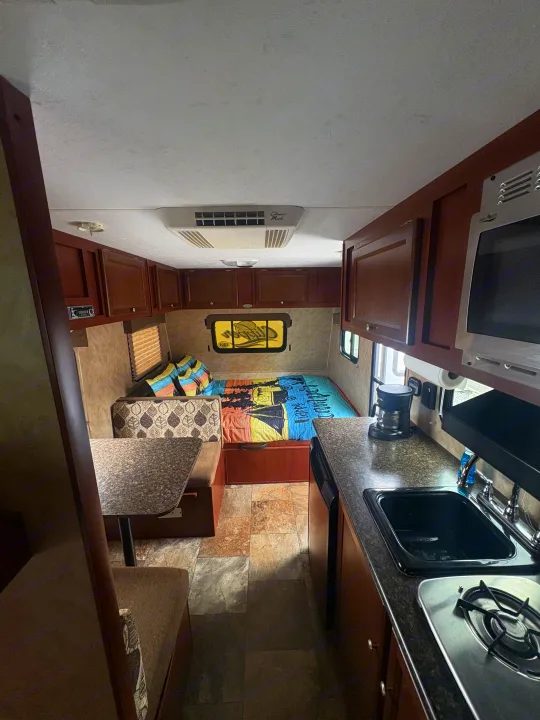 RV rental interior: cozy kitchen, dinette, and bed setup with overhead cabinets and AC. Ready for adventure!. Coachmen Clipper 17BH 2015