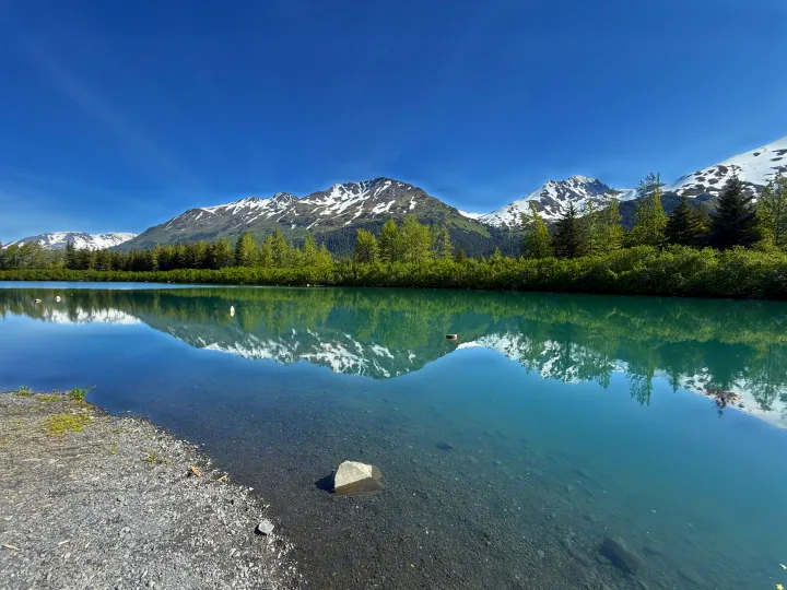 Enjoy this scenic view of snow-capped mountains reflecting in a clear lake, ideal for an RV rental trip. Nature's beauty awaits!. Heartland RVs Prowler Lynx 2024