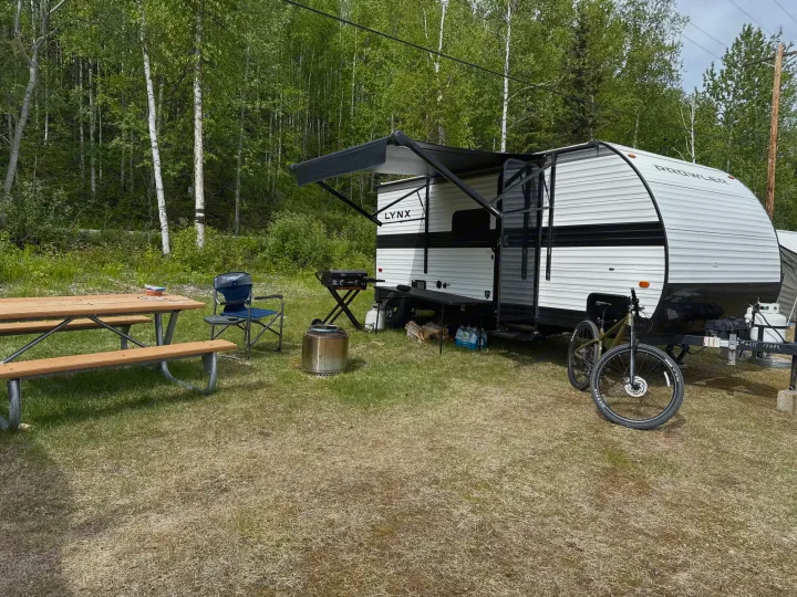 Relaxing at an RV rental campsite. Features a travel trailer with awning, picnic table, grill, Solo Stove, and bicycle.. Heartland RVs Prowler Lynx 2024
