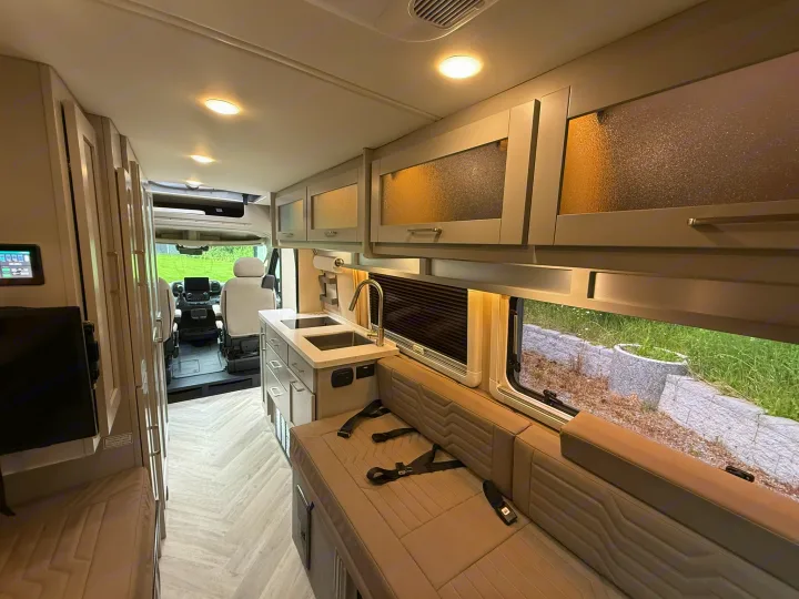 Bright RV rental interior showing a modern kitchen, comfortable seating with belts, and stylish frosted overhead cabinets.. Coachmen Nova 2024