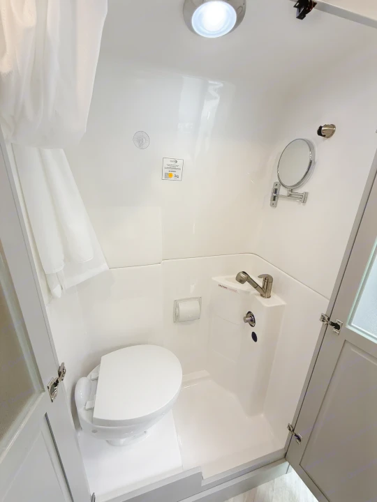 Compact RV rental's white bathroom features a toilet, integrated sink/shower combo, mirror, and bright overhead light.. Coachmen Nova 2024