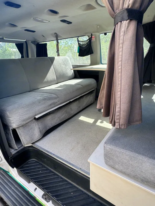 Cozy RV rental interior: grey bench seat (converts to bed), small table, & privacy curtains, ready for your road trip.. Ford Econoline 150 2012