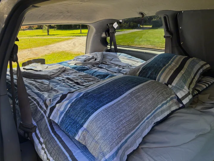 Inside a cozy RV rental: a comfy bed with striped pillows & blankets, ready for your next road trip adventure.. Dodge Grand Caravan 2005