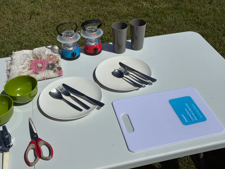 RV rental camping gear: A table set with plates, cutlery, bowls, cups, lanterns, and a cutting board for outdoor dining.. Dodge Grand Caravan 2005