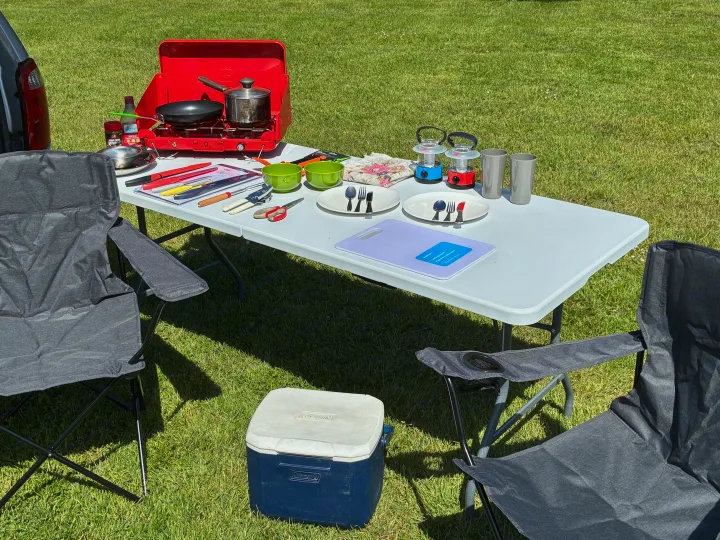 RV rental adventure: An outdoor cooking setup with a portable stove, table, chairs, cooler, and kitchenware on grass.. Dodge Grand Caravan 2005