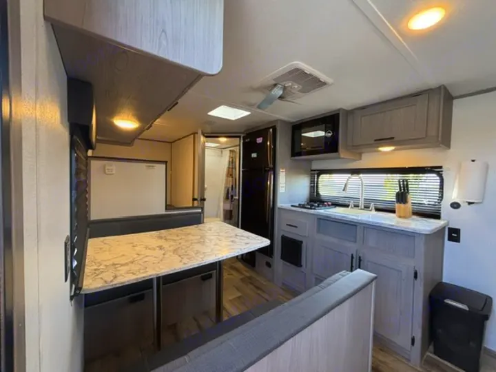 RV rental interior: modern kitchen with sink, stove, microwave, fridge, gray cabinets, and a marble-top dinette.. Dutchmen Coleman Lantern LT 2024