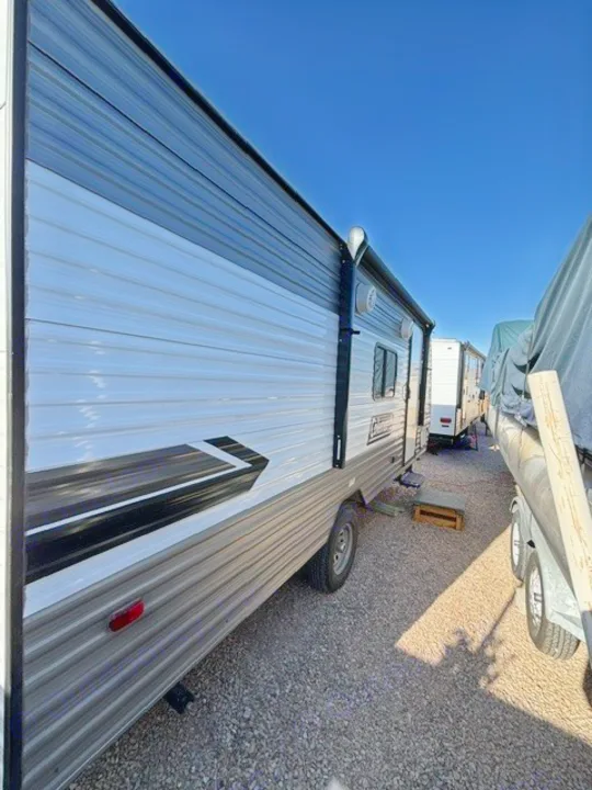 A clean, modern RV rental travel trailer with white and dark gray siding, graphic accents, and an awning, parked outdoors.. Dutchmen Coleman Lantern LT 2024