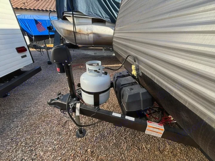 Front hitch assembly of an RV rental travel trailer, featuring a propane tank, battery box, and power jack on gravel.. Dutchmen Coleman Lantern LT 2024