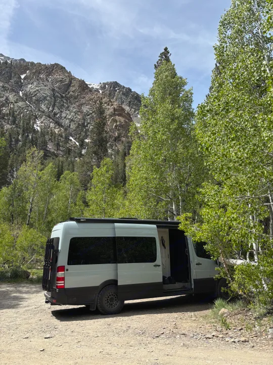 Scenic RV rental adventure: a camper van nestled on a dirt path, surrounded by vibrant green aspens and majestic snow-dusted mountains.. Mercedes-Benz Sprinter RV Motorhome Campervan 2012