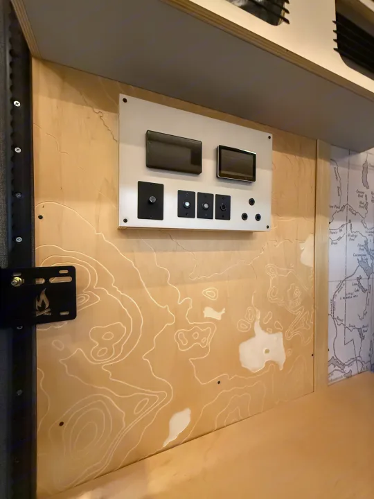RV rental interior showcasing a modern control panel mounted on a custom wood wall with a carved topographical map design.. Ford Transit 2025