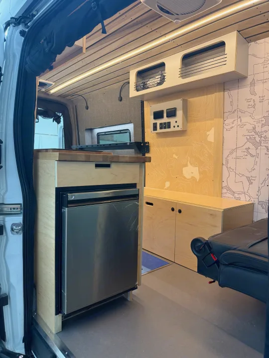 RV rental camper van interior: kitchen with fridge, wood paneling, overhead storage, and control panel, ready for adventure!. Ford Transit 2025