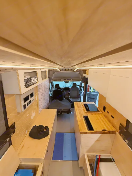 Interior of a custom rv rental camper van, showing a wooden kitchen, storage, and front cabin view.. Ford Transit 2025