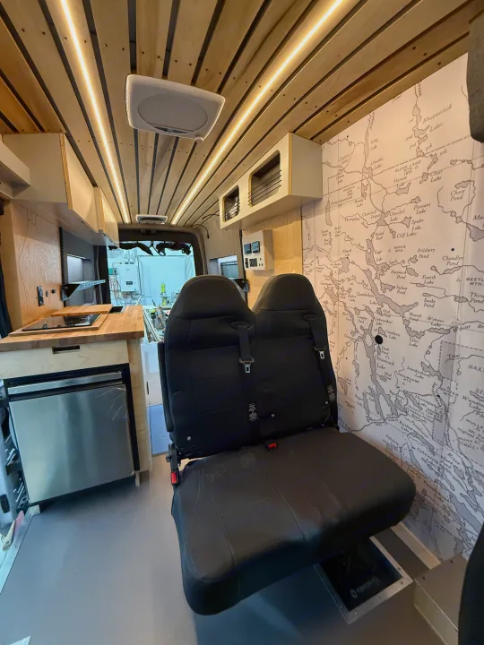 Modern rv rental camper van interior: custom kitchen, integrated fridge, comfortable seating, and illuminated wood slat ceiling.. Ford Transit 2025