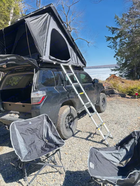 Black SUV with a deployed roof top tent by a frozen lake, ideal for an RV rental camping getaway in nature.. Toyota 4Runner 2014