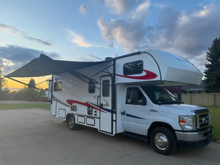 White Class C rv rental with awning extended, parked outdoors at sunset. Ready for adventure and travel.. Forester 2501CD 2023