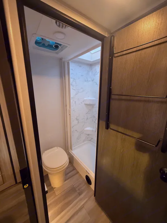 This RV rental's compact bathroom features a toilet, modern tiled shower with a skylight, and space-saving door storage.. Forester 2501CD 2023