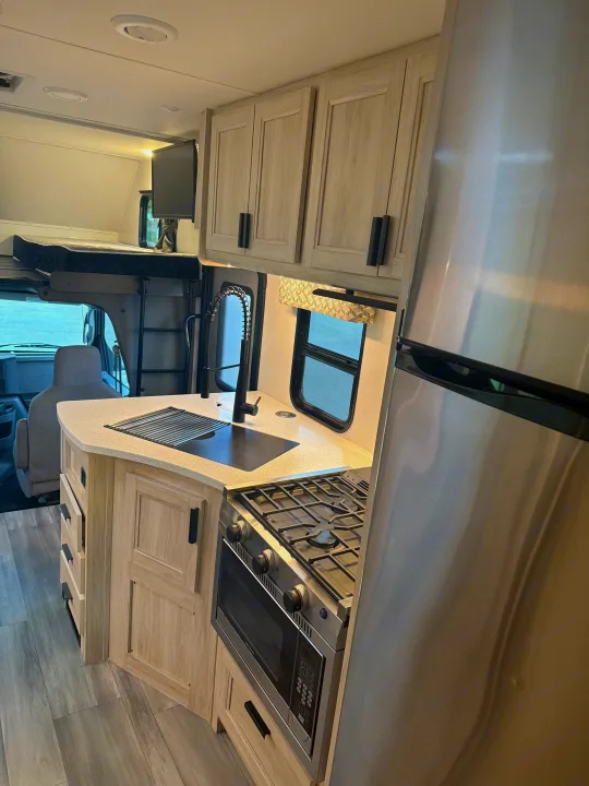 Explore this well-equipped RV rental interior: kitchen with stove, oven, fridge, sink, light cabinets & an over-cab bed area.. Forester 2501CD 2023