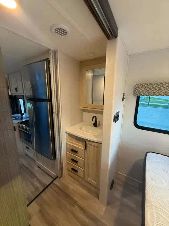 Inside a modern RV rental: a compact kitchen, bathroom vanity with sink & mirror, and a cozy bed area.. Forester 2501CD 2023