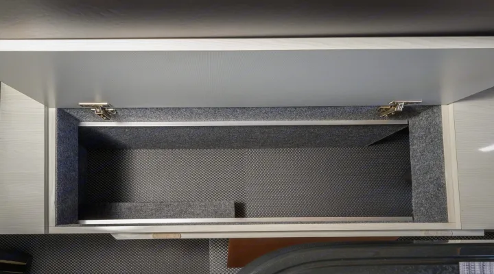 Open overhead cabinet in an RV rental, featuring carpeted walls and a textured non-slip mat at the bottom for secure storage.. Other Gala Montecarlo 2025