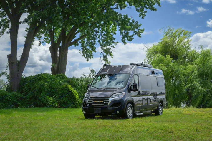 Sleek black RV rental parked in a green field with lush trees and a blue, cloudy sky, perfect for outdoor adventures.. Other Gala Montecarlo 2025