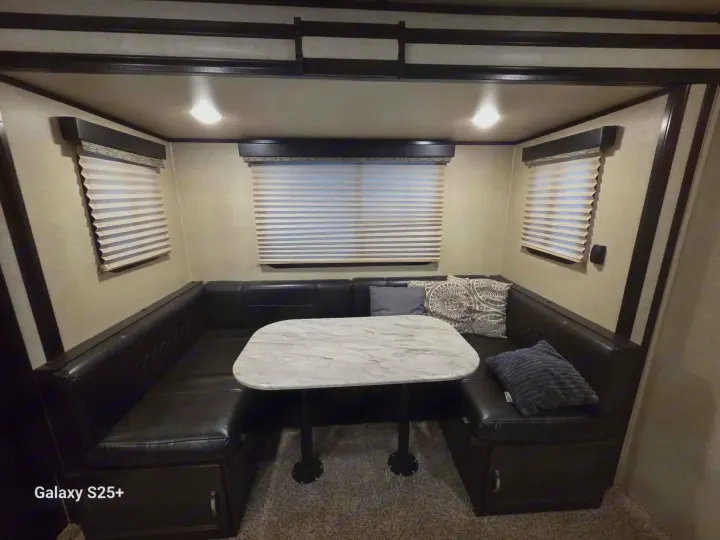 Spacious RV rental dinette featuring a U-shaped black leather booth, a light marble-style table, and bright overhead lights.. Coachmen Spirit ultra lite 2019