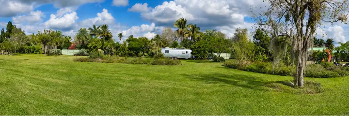A silver Airstream-style rv rental is nestled in a lush green park, surrounded by tropical trees under a partly cloudy sky.. Airstream Flying Cloud 2019