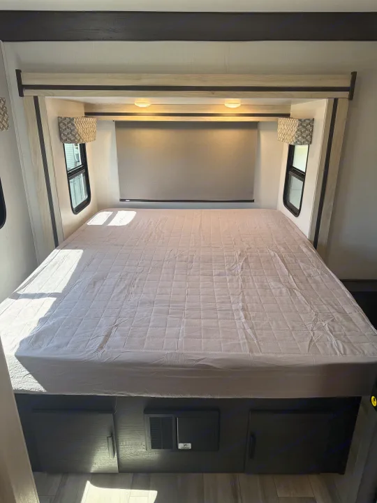 RV rental bedroom: a large bed with quilted mattress, side windows, overhead lights, and under-bed storage. Sunlight filters in.. Forester 2501CD 2023