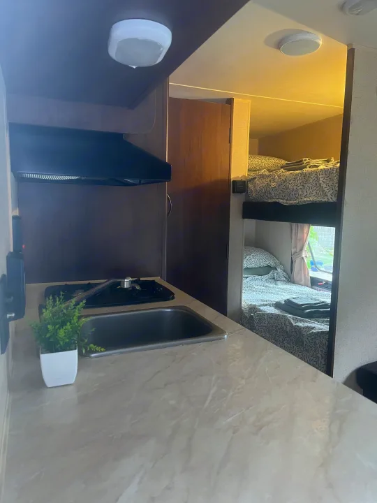 Cozy RV rental interior featuring a compact kitchen with stove and sink, plus comfortable bunk beds.. Jayco Jay Flight 2015