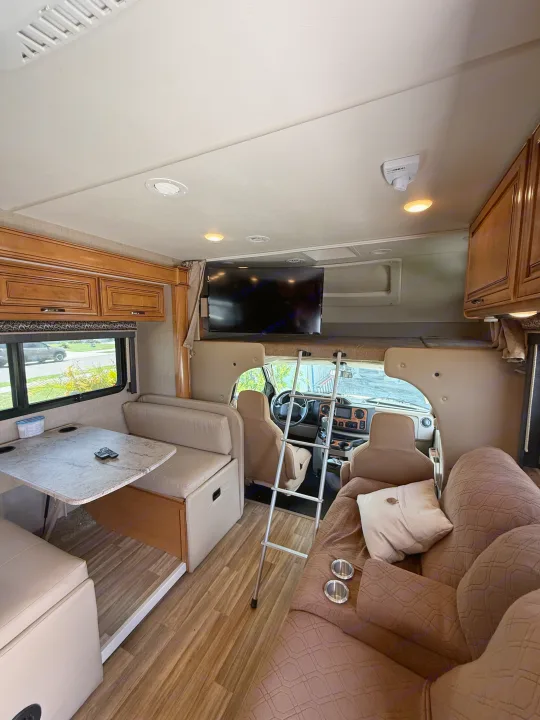 Spacious rv rental interior featuring a dinette, cozy sofa with cup holders, overhead TV, and cab-over bunk area.. Thor Quantum 2017