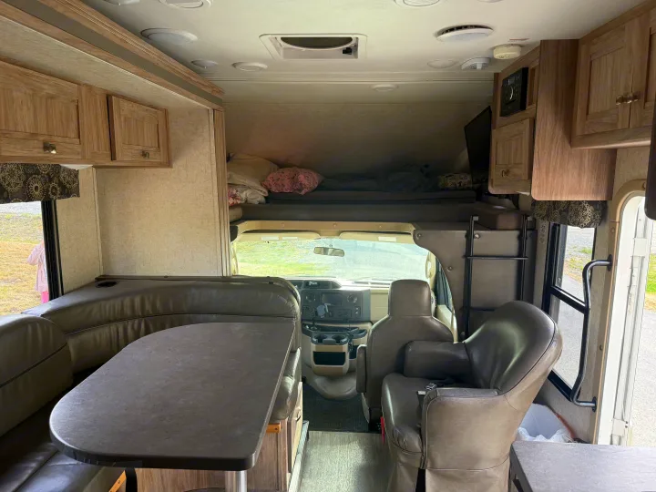Inside this RV rental: comfy dining area, overhead bunk, and cockpit view. Perfect for your next road trip adventure!. Forest River Sunseeker 2018