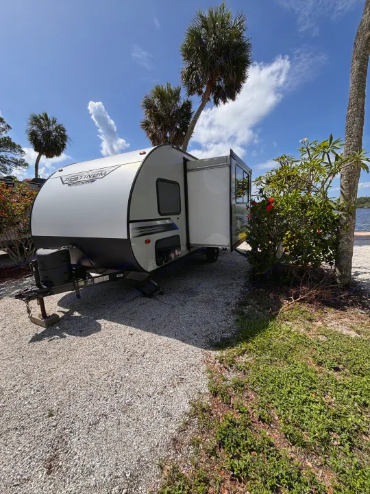 White and gray Forest River Platinum rv rental travel trailer parked on gravel, surrounded by palm trees with a water view.. Forest River Salem FSX PLATINUM 2020