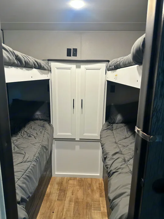 RV rental bunk bed area featuring two sleeping berths with gray bedding, a central white cabinet, and power/TV outlets.. Keystone RV Hideout 2022