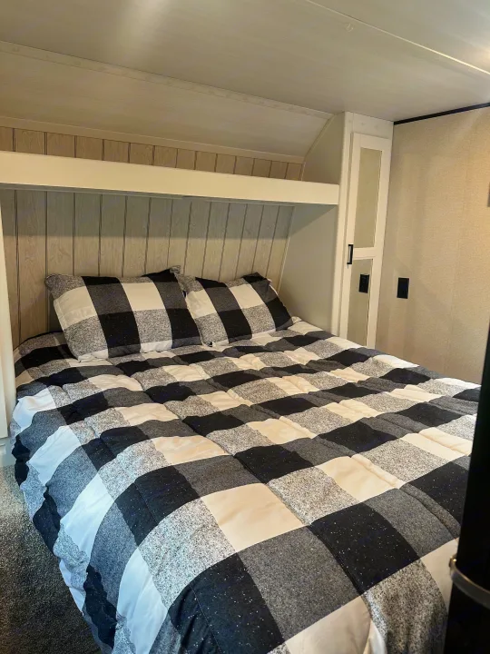 Cozy RV rental bedroom featuring a black, white, and gray checkered bed, built-in storage, and paneled headboard.. Keystone RV Hideout 2022
