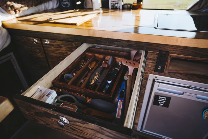 Inside an RV rental: a neat kitchen drawer with utensils & an Aeropress, next to a Dometic fridge. Efficient camper storage.. Dodge 1500 2020