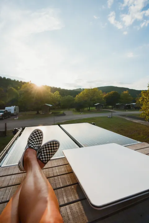 Relaxing from an RV rental, feet in checkered shoes propped on a deck, with solar panels and a sunny campground view.. Dodge 1500 2020