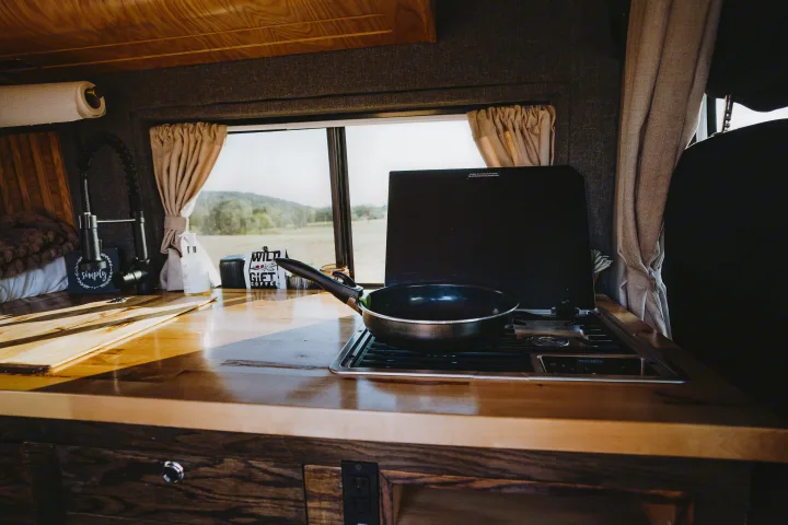 Experience van life in this RV rental's functional camper kitchen with a Dometic stove, sink, wooden counter, and scenic view.. Dodge 1500 2020