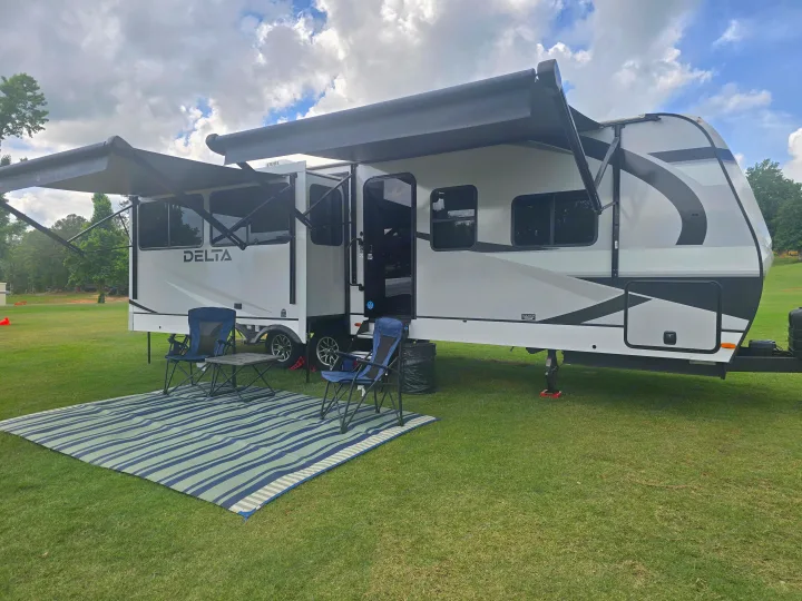 Spacious DELTA RV rental with extended awnings, outdoor mat, and chairs on a grassy campsite for a comfortable getaway.. Alliance Delta 292RL 2025