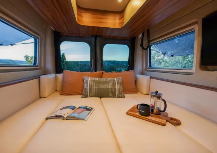Cozy rv rental interior showing a comfortable lounge area, open book, and coffee with a scenic view outside.. Noovo Plus LB 2025