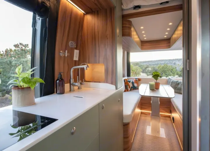 Modern RV rental features a compact kitchen with a sink and cooktop, plus a cozy dining area, highlighted by warm wood accents.. Noovo Plus LB 2025
