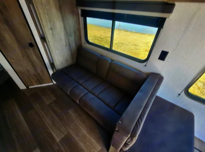 Cozy RV rental interior featuring a comfortable gray sofa, large window with blinds, and modern wood-look flooring.. Sunset Park RV Sun Lite 2026
