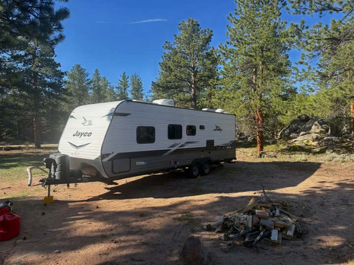 Jayco travel trailer RV rental at a sunny pine forest campsite with firewood. Perfect for camping and outdoor adventures.. Jayco Jay Flight SLX 2022